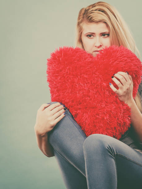 istock Sad woman holding red pillow in heart shape 884149146