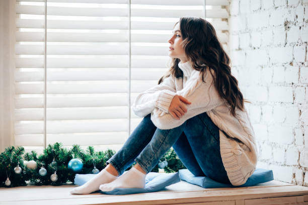 young beautiful woman relaxing on window sill in christmas decorated home. - sensuality lifestyles cheerful comfortable imagens e fotografias de stock