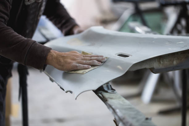 Car repair jobs Car detailing - Man with sandpaper in auto repair shop sanding polishing and preparing car parts for painting. Selective focus on man's hand. bodywork stock pictures, royalty-free photos & images