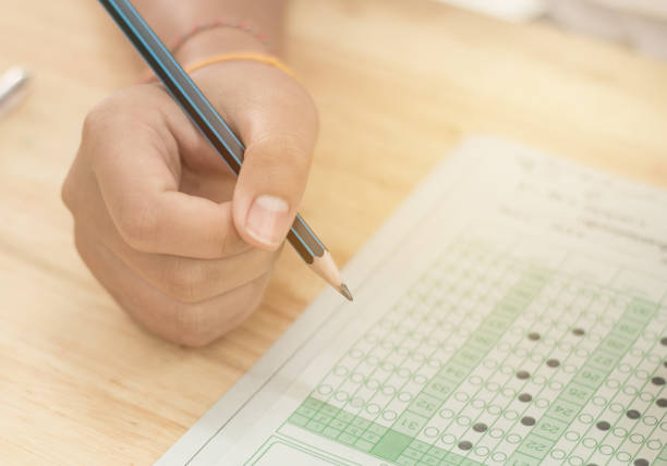 istock Asian Students holding pencil in hand doing multiple-choice quizzes or testing exams answer sheets exercises on old wood table In secondary school, college university classroom in education concept 884161284