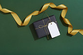 Gift tag, Christmas gifts and gold ribbon on dark green background, flat lay