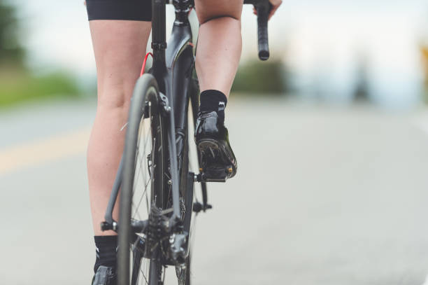 female cyclist rides along a rural highway - road cycling imagens e fotografias de stock