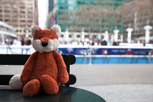 A plush stuffed fox sits at a table, at Bryant Park by the ice rink.