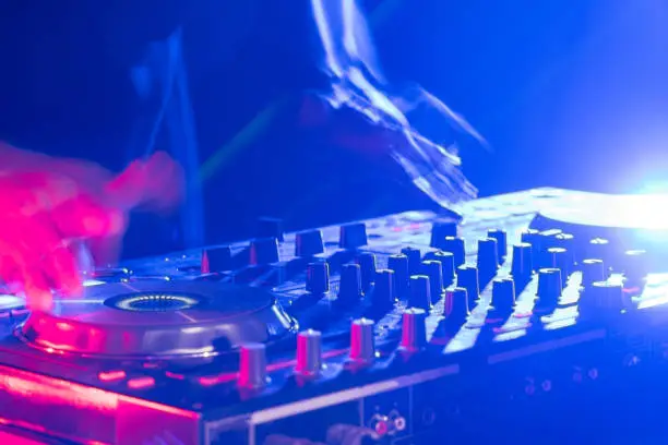 Motionblur of Dj hands on equipment deck and mixer with vinyl record at party.Closeup.