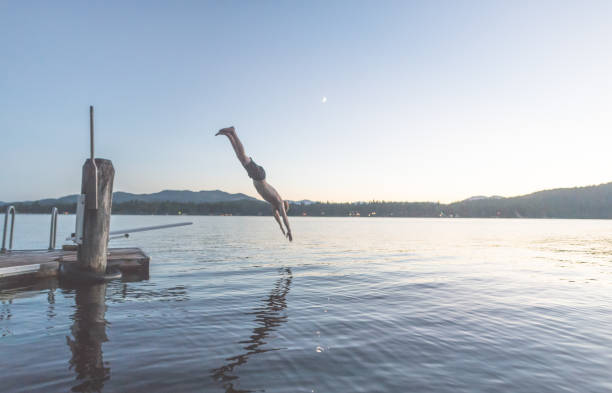 istock Young man dives into a lake off pier at dusk 884333194