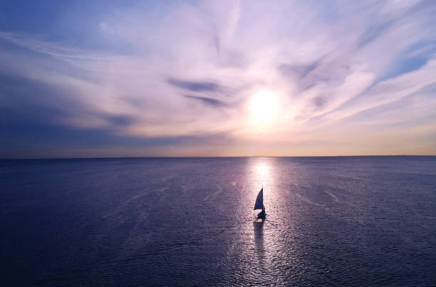 cornice romantica: yacht che galleggia in lontananza verso l'orizzonte nei raggi del sole al tramonto. tramonto viola-rosa - horizon over water environment vacations nature foto e immagini stock