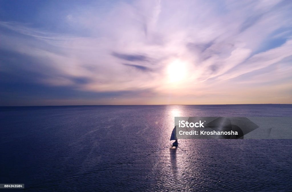 Romantic frame: yacht floating away into the distance towards the horizon in the rays of the setting sun. Purple-pink sunset Sailboat Stock Photo