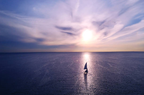 Romantic frame: yacht floating away into the distance towards the horizon in the rays of the setting sun. Purple-pink sunset stock photo