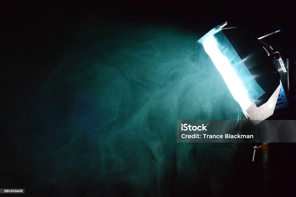 smoke around a filtered light on a film set a side view of a filtered light through smoke effects on a dark film set Film Set Stock Photo