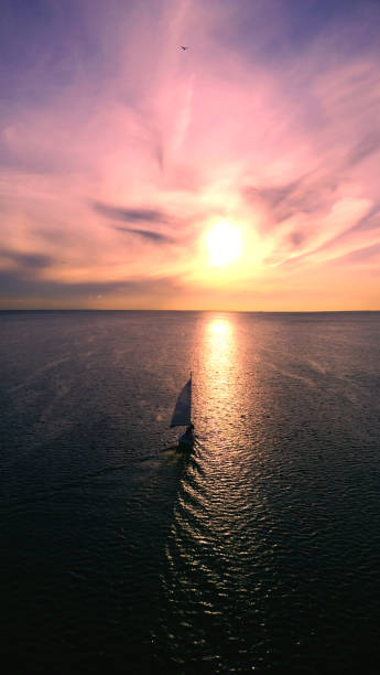 Beautiful little boat floats toward the horizon on the background of the sunset coloured sky. The view from the air. Vertical view stock photo