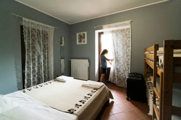 Teen girl looks out the window of a guest room at La Porta farm in Anversa village in Abruzzo, Italy, Europe