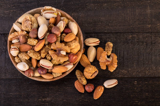 Organic Raw Nuts Mix Of Pistachios, Almonds, Walnuts, Dried Mulberries, Dried Figs And Hazelnuts On Wooden Plate And Table Background Top View Of Organic Raw Nuts Mix Of Pistachios, Almonds, Walnuts, Dried Mulberries, Dried Figs And Hazelnuts On Wooden Plate And Table Background, Healthy Natural Trail Mix Snack, Shot From Above nut variation healthy lifestyle pistachio stock pictures, royalty-free photos & images