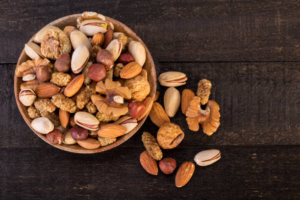 organic raw nuts mix of pistachios, almonds, walnuts, dried mulberries, dried figs and hazelnuts on wooden plate and table background - peanut food snack healthy eating imagens e fotografias de stock