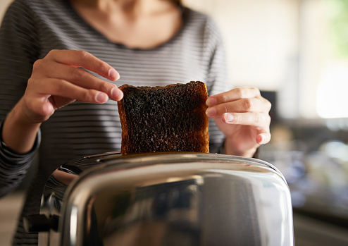 Cropped shot of a woman removing a slice of burnt toast from a toaster at home