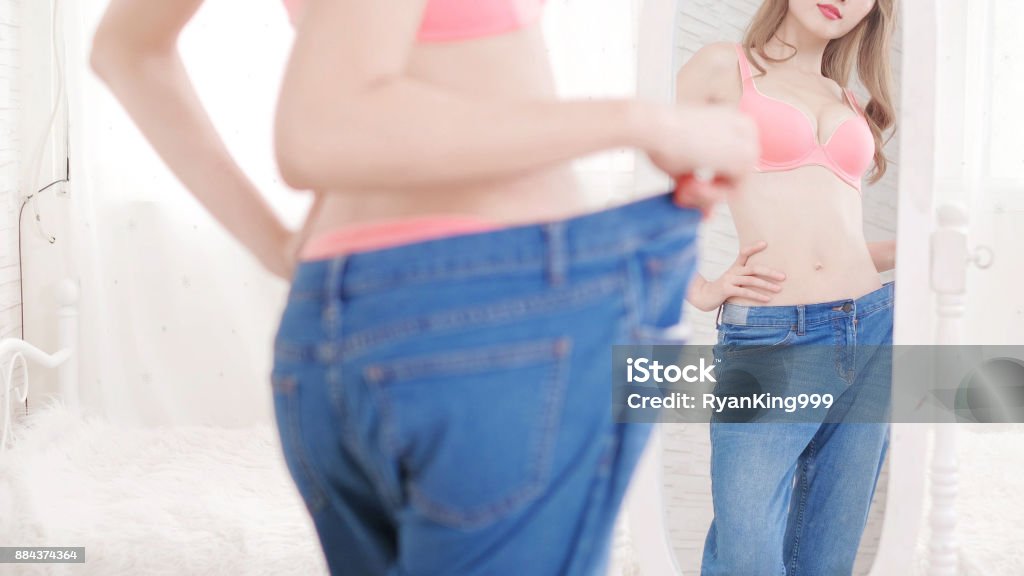 weight loss concept Happy slim woman look her old jeans in the mirror at home Dieting Stock Photo