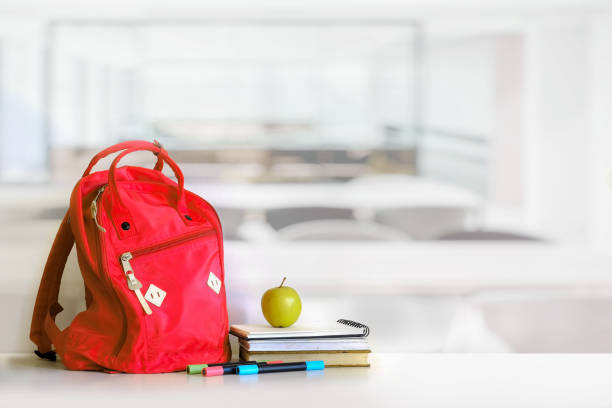 Red backpack and books school supplies in classroom.