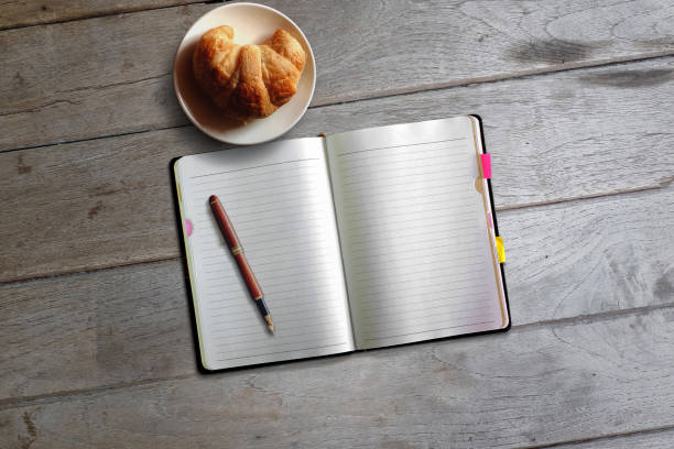 istock Top view open notebook, pen and croissant on wood desk background. 884374900