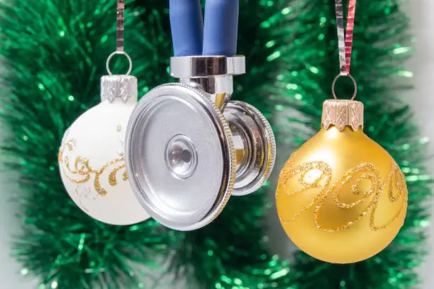 Medical Christmas and New Year. Stethoscope surrounded by white and gold christmas tree balls with blurred christmas decoration on background - green garlands. Concept for the New Year in medicine