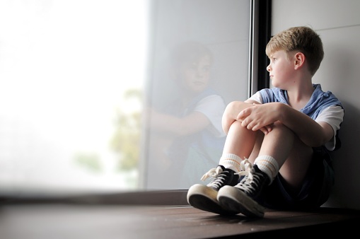 Young boy sits looking out a window.