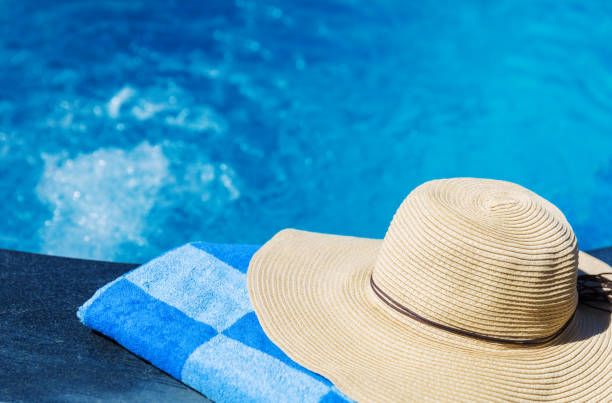istock Straw hat and blue towel near swimming pool 884480256