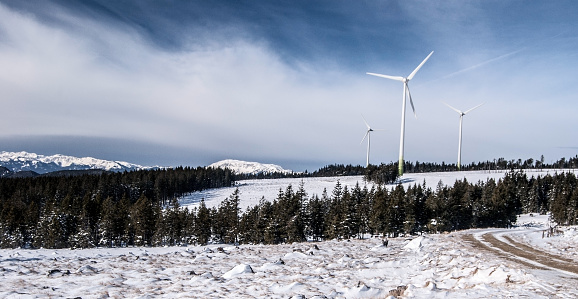 winter Fischbacher Alpen mountain range in Austria with snow, forest,  wind turbines and higher peaks on the background