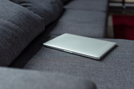 close up view of closed laptop lying on grey sofa