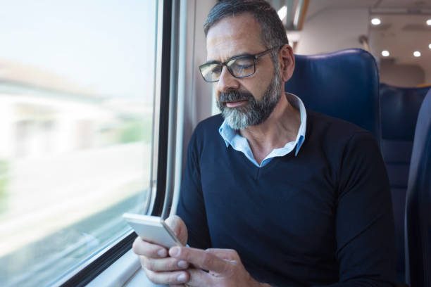 istock Mature man in train travelling using mobile phone 884498126