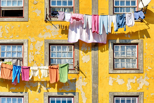 Picturesque yellow building facade with peeling paint and colorful clothes lines in historic Porto, Portugal.