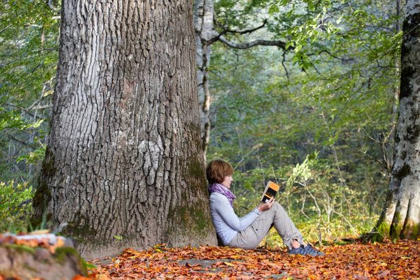 istock A girl is reading a book sitting by a tree 884531614
