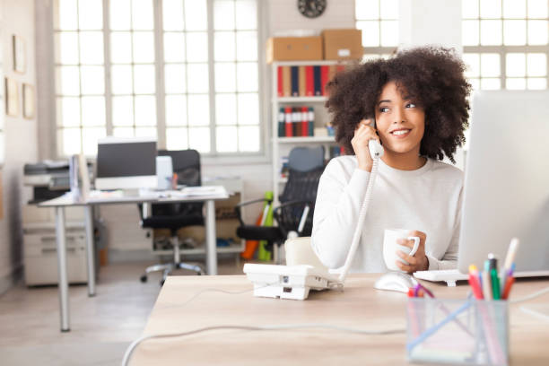 istock Smiling female assistant using landline phone in modern office 884564478