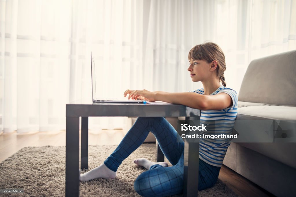 Teeange girl doing homework at home Teenage girl is using her modern lightweight ultrabook for homework research. Girl is sitting on the floor by small table.
 Teenager Stock Photo
