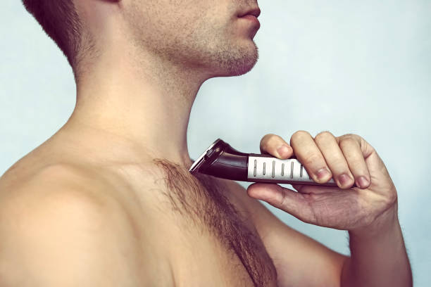 Handsome young bearded man with Handsome young bearded man with a trimmer shaving off body hair semi dress stock pictures, royalty-free photos & images