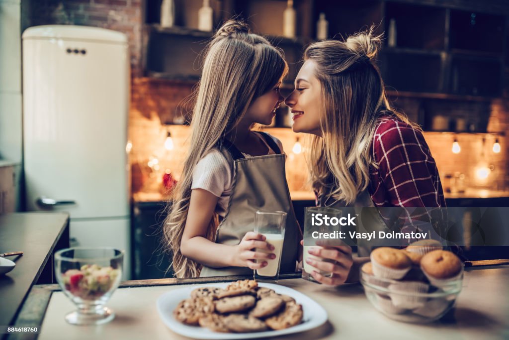 Mom with daughter on kitchen. Attractive young woman with her little cute daughter are cooking on kitchen. Drinking milk, eating cakes and cookies. Mother Stock Photo