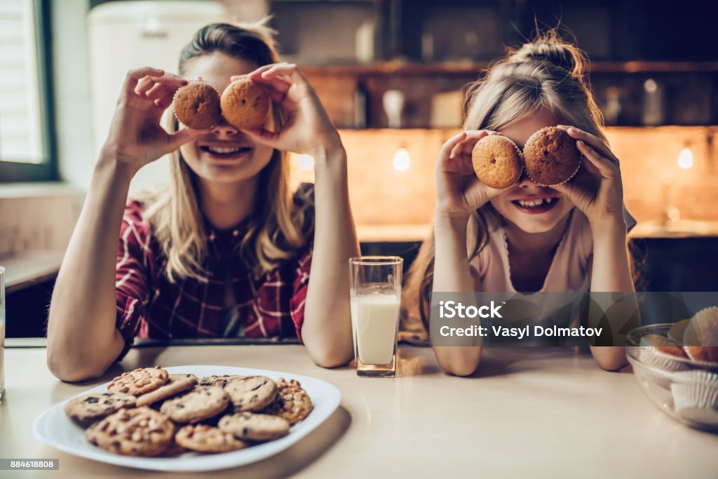 Mom with daughter on kitchen. Attractive young woman with her little cute daughter are cooking on kitchen. Drinking milk, eating cakes and cookies. Child Stock Photo
