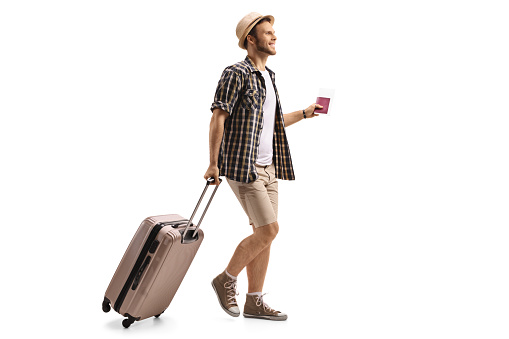 Full length profile shot of a tourist with a passport and a suitcase walking isolated on white background