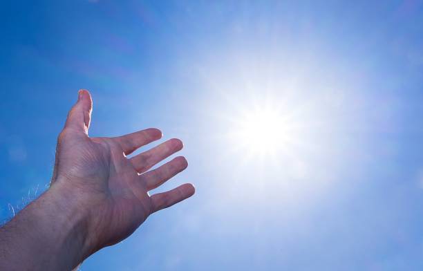 istock Hand held up to blue sky toward sun and heaven 884638172