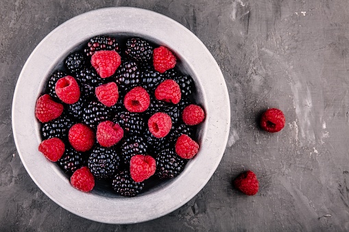 fresh ripe organic raspberries and blackberries in a bowl on a gray rustic background