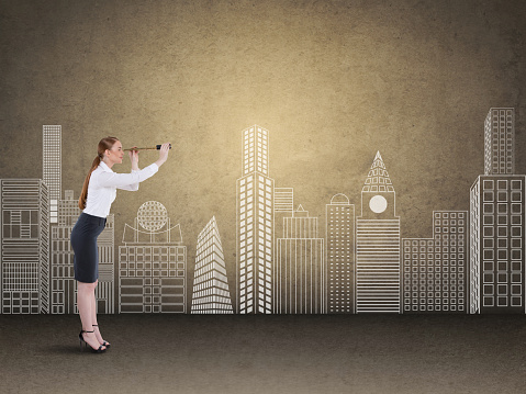 Businesswoman looking through spyglass in front of city buildings