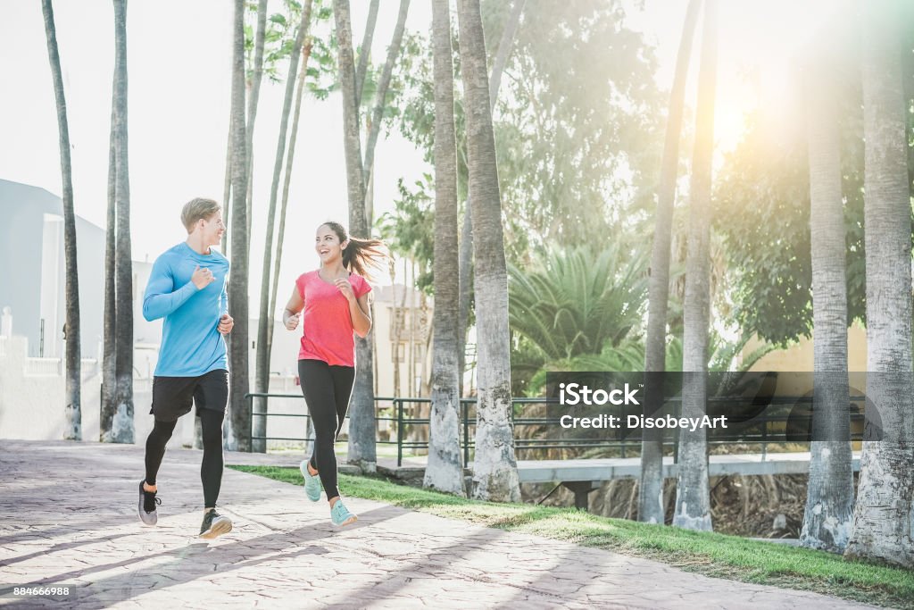 Fitness young couple running outdoor with palms in background - Sporty happy people training in tropical place - Healthy lifestyle, happiness, jogging and vitality concept - Warm filter People Stock Photo