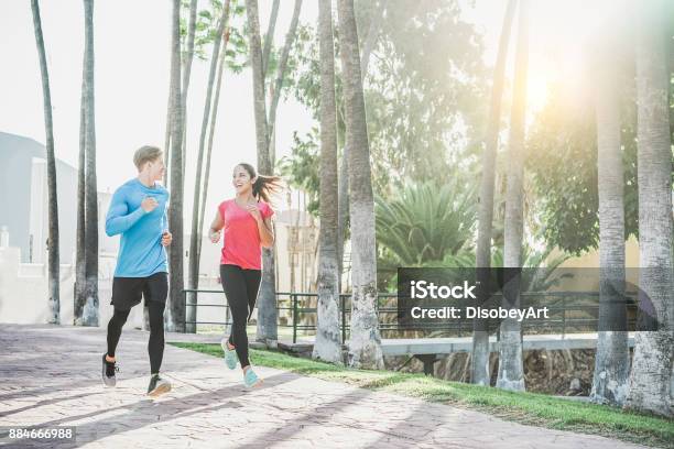 Fitness Young Couple Running Outdoor With Palms In Background Sporty Happy People Training In Tropical Place Healthy Lifestyle Happiness Jogging And Vitality Concept Warm Filter Stock Photo - Download Image Now