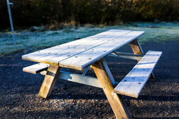 White frost ice crystals on wooden picnic table in morning sunlight by forest and campground park
