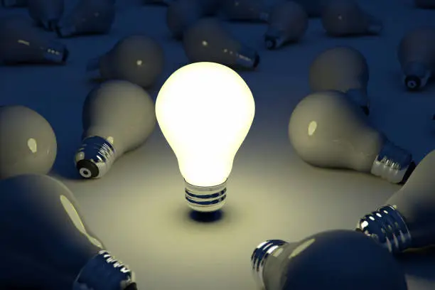 One light bulb illuminated with others dark.  The business concept image illustrates bright idea or standing out of the crowd.