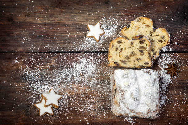istock christmas background, traditional german criststollen cake sprinkled with icing sugar, cinnamon cookies and anise stars on a dark rustic wooden board, top view from above, copy space 884736760