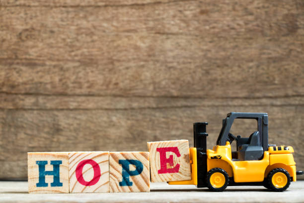 istock Yellow plastic toy forklift hold letter block E to complete word hope on wood background 884736854