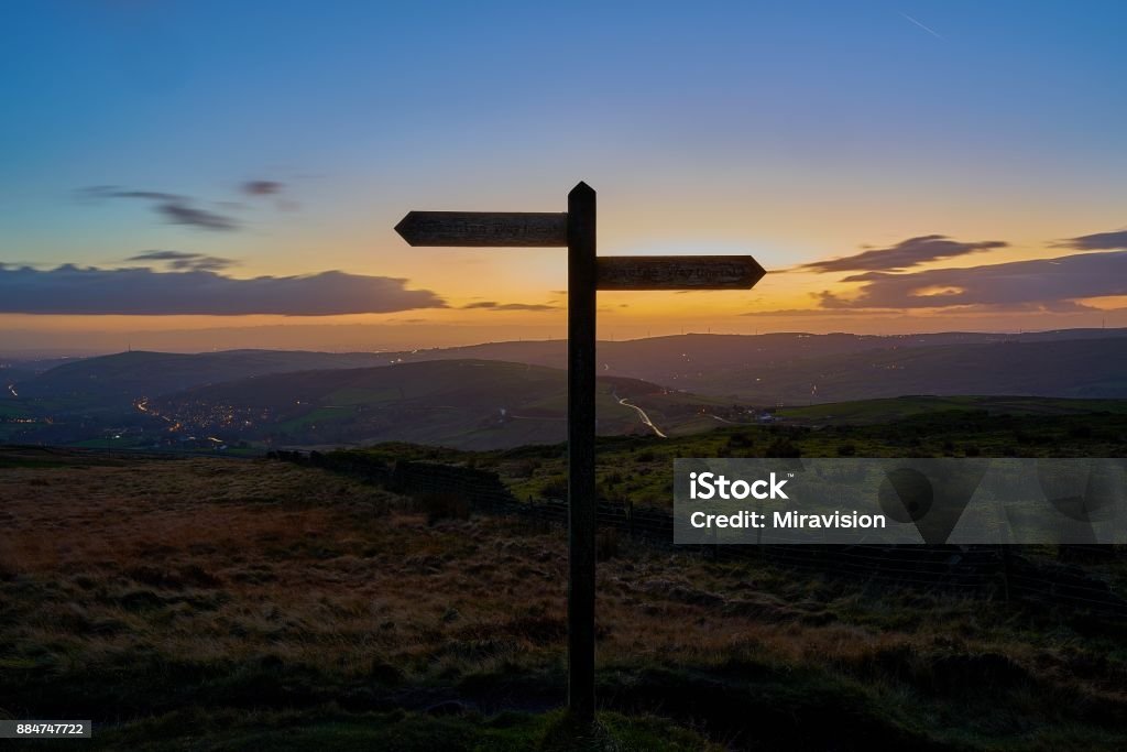 North-south signpost silhoutte. North-south sign on hilltop trail with an orange dusk sky in the background. Road Sign Stock Photo