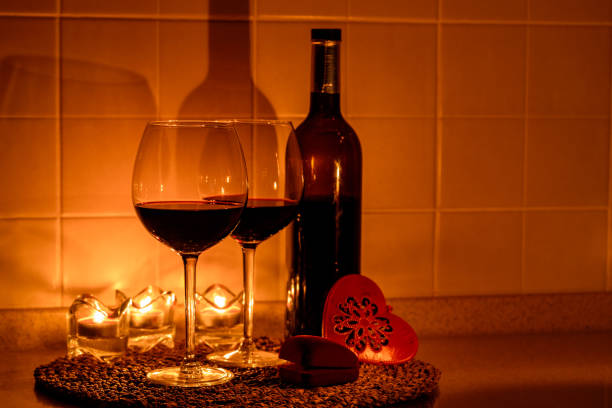 Glass of red wine and bottle of wine, against a dark background.