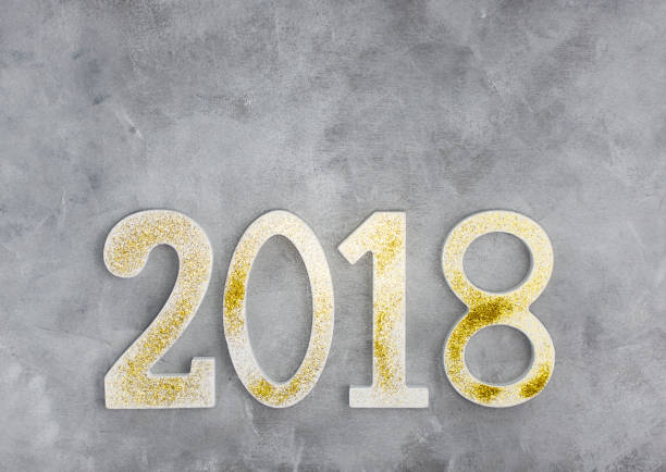 istock Luxury glowing numbers 2018 made from gold shiny glitter on grey concrete table 884826726