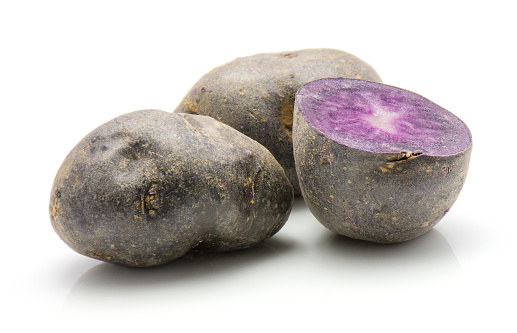 Two vitelotte potatoes and one purple half isolated on white background\