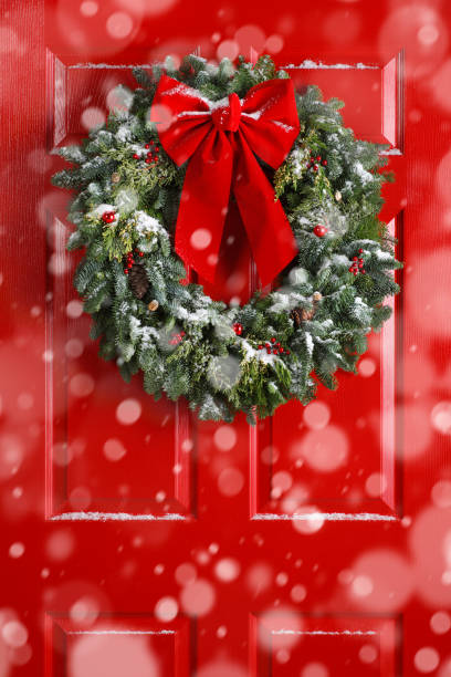 istock Snow Falling In Front Of Red Door Adorned With Wreath 884933102