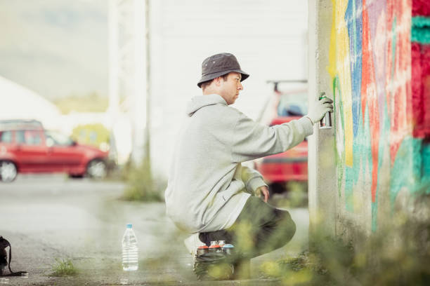 istock Young Graffiti Artist Spraying Graffiti on Wall 884972024